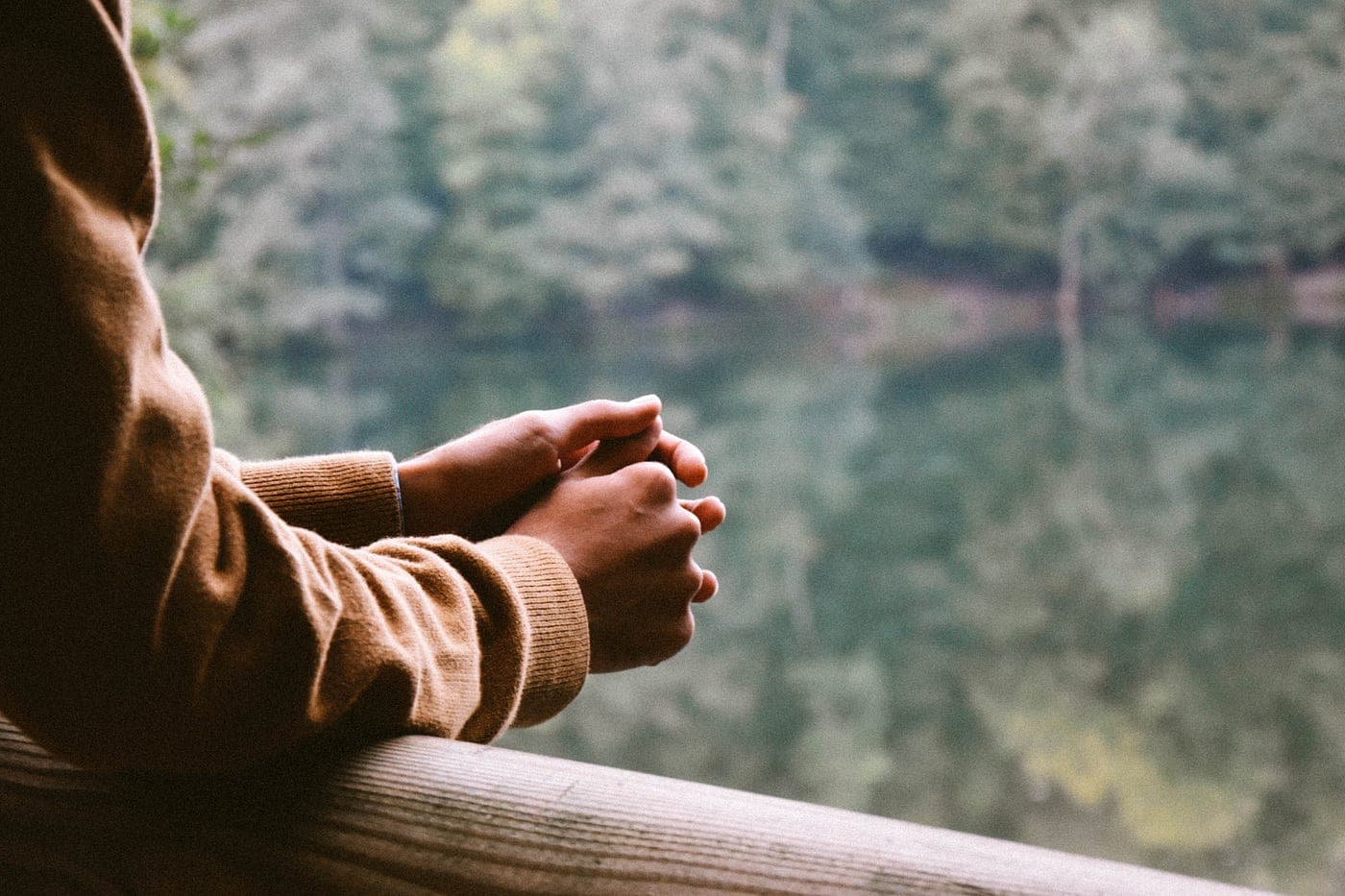 arms held pensively on a rail before a blurred background of trees and a lake
